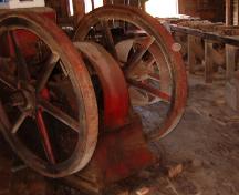 The first engine used in the mill, started by cranking the big fly-wheel and adding gasoline; used for 40 years.  This engine was later replaced by a diesel engine.  Photo taken during Doors Open Placentia event 2006.; HFNL/ 2006