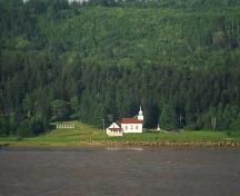 Prise du côté opposé de la rivière Petitcodiac, cette photo montre la chapelle Sainte-Anne, le presbytère et une partie du cimetière.; La Société historique de la Valleé de Memramcook