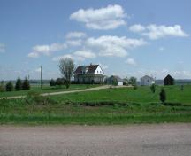 Maison natale de Roméo LeBlanc - Prise de la route principale, cette vue éloignée montre l'emplacement de la maison, face à l'ouest, avec le coteau élevé de Memramcook-est à l'arrière-plan; Gérard LeBlanc