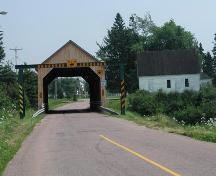 Vue lointaine, prise du nord-ouest, montrant l'emplacement de l'école tout près du pont couvert de Gayton qui enjambe la rivière Memramcook.; Gérard LeBlanc