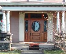 Cette image montre une vue de l'entrée flanquée par des pilastres corinthiens et comprenant une imposte en vitrail, des fenêtres latérales et une porte en bois à panneau de verre arrondi, 2006; City of Saint John