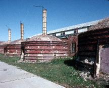 Vue générale des poteries Medalta, qui montre les fours ronds avec leurs extérieurs en brique, les lanterneaux continus, et les bardeaux de bois des toits.; Parks Canada Agency / Agence Parcs Canada.