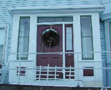 Cette image montre l'entrée centrale fermée avec un toit à pente faible, une imposte à quatre panneaux et des fenêtres latérales à deux panneaux, 2006; City of Saint John