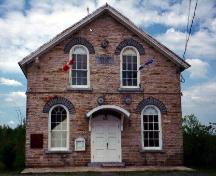 General view of Havelock Township Hall, showing its simple classical composition, as seen in its symmetrically placed windows on the front façade, its gable roof, regularly placed openings, and central entrance.; Parks Canada Agency / Agence Parcs Canada.