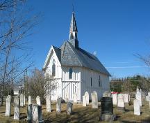 This image presents the context of the building surrounded by cemetery stones nestled in a churchyard in what still can be considered a rural community setting.; PNB 2005