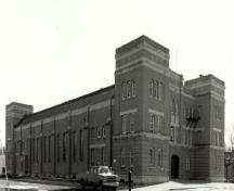 Vue en angle du manège militaire de la rue McGregor, où l'on peut apercevoir l’échelle et le volume monumental du bâtiment formé d’un bloc principal, de tours d’angle carrées solides, 1994.; Department of National Defence / Ministère de la Défense nationale, 1994.