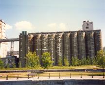 Vue de l'extérieur de l'annexe, qui montre la volumétrie formée de 10 hauts cylindres de béton, collés les uns aux autres pour former une paroi continue, et l’étage vitré qui surmonte l’ensemble, 1995.; Parks Canada Agency / Agence Parcs Canada, J. Hallé, 1995.