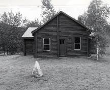 View of the main entrance to the N.W.M.P. Jail, showing the log construction of peeled local spruce logs, sawn on three sides and lapped at the corners, 1987.; Agence Parcs Canada / Parks Canada Agency, 1987.