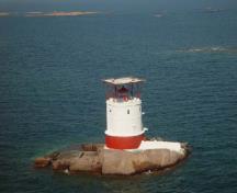 Vue générale du phare du rocher Red, qui montre le contraste offert par les textures et les couleurs des plaques d’acier rivetées rouges de la base et des murs en béton blanc, lisses, au-dessus.; Canadian Coast Guard / Garde côtière canadienne.