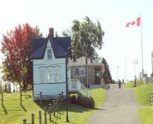 Façade latérale de la logette 1, qui montre les murs blancs du bâtiment, revêtus d’un parement en bois.; Parks Canada Agency / Agence Parcs Canada.