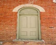 Vue de l'extérieur de l'ancienne école de rang d'Atha, qui montre le lambri supérieur semi-circulaire de la porte, 2005.; Department of Public Works and Government Services / Ministère des Travaux publics et services gouvernementaux, Alice Da Silva, 2005.