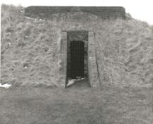 Vue de la poudrière de l'est, qui montre l'entrée protégée, flanquées de murs latéraux en brique qui descendent jusqu’au niveau du sol, 1989.; Parks Canada Agency / Agence Parcs Canada, 1989.