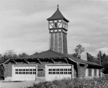 Vue de la Caserne de pompiers montrant la construction de rondins complexe, l’abri en bois qui renferme le garage et le comble en croupe, et illustre clairement la visibilité de la tour.; Parks Canada Agency / Agence Parcs Canada, n.d.