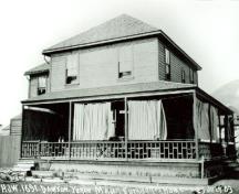 Vue de la façade latérale de la résidence du commandant, qui montre un toit en croupe bas recouvert de bardeaux, avec des contours précis, et une véranda qui court sur toute la longueur du bâtiment, 1903.; Library and Archives Canada/ Bibliothèque et Archives Canada, 1903.
