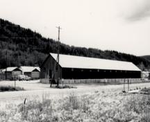 Vue de l’entrepôt de la Northern Commercial Company, qui montre les nombreuses petites fenêtres régulièrement espacées sur les longs murs immédiatement sous la sablière, 1987.; Agence Parcs Canada / Parks Canada Agency, 1987.