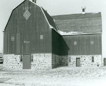 Vue générale de la Grange, montrant la forme de L du bâtiment de trois étages couvert d’un toit en mansarde et construit en pierre et en bois, 1988.; Agence Parcs Canada, Homestead Motherwell/ Parks Canada Agency, Motherwell Homestead, 1988.