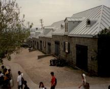 Vue du hangar à affûts de canon, qui montre le toit en croupe recouvert de tôle à baguette et les lucarnes semi-circulaires au-dessus des portes, 1991.; Agence Parcs Canada / Parks Canada Agency, 1991.