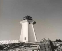 Vue générale du Phare à la pointe Atkinson, où l'on peut apercevoir la haute tour hexagonale flanquée de contreforts nervurés avec une vaste plate-forme, un fanal circulaire et un grand dôme hémisphérique, 1990.; Canadian Coast Guard / Garde côtière canadienne, 1990.