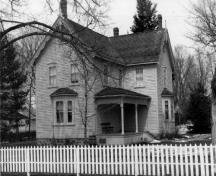 View of the south façade of Bethune House, showing the clapboard exterior walls, the symmetrical arrangement of the windows, the bay windows and the verandah, 1989.; Agence Parcs Canada / Parks Canada Agency, 1989.