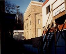 View of the Transformer House, showing its brick massing, flat roof, and well-defined concrete foundation, 1991.; Travaux publics Canada / Public Works Canada, 1991.