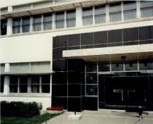 View of the main entrance to Building M-20, showing the use of smooth "modern" materials such as steel, glass block, white stucco and black marble veneer, 1991.; Parks Canada Agency / Agence Parcs Canada, J. Adell, 1991.