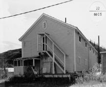 Corner view of the Mess Hall and Bunkhouse, showing the arrangement and detailing of its doors and windows, its porches, and its covered stair, 1988.; Parks Canada Agency / Agence Parcs Canada, 1988.