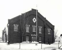 General View of the Armoury, showing its load bearing exterior walls clad in red brick with engaged pilasters and detailed with flat-voussoired windows, 1989.; Department of National Defence / Ministère de la Défense nationale, 1989.