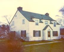 Façade de la résidence du directeur du parc, qui montre le volume simple et le plan symétrique du bâtiment qui consiste en un bâtiment de deux étages, coiffé d’un toit à deux versants, 1990.; Parks Canada Agency / Agence Parcs Canada, 1990.