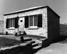 General view of Building 16, showing the small, rectangular, one-storey massing with a low hipped roof, 1980.; Parks Canada Agency / Agence Parcs Canada, 1980.