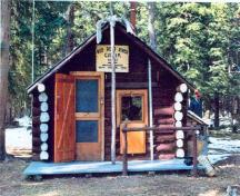 Vue de l'entrée principale du chalet des gardes du parc de Sandhills, qui montre la porte d’entrée décalée et équilibrée par une fenêtre, 1996.; Agence Parcs Canada / Parks Canada Agency, 1996.