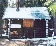 Façade latérale de le chalet des gardes du parc de Sandhills, qui montre la construction en rondins rustiques assemblés en sabot, 1996.; Agence Parcs Canada / Parks Canada Agency, 1996.