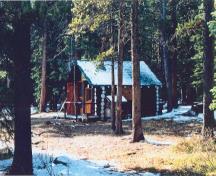 Vue en angle du chalet des gardes du parc de Sandhills, qui montre le plan rectangulaire et le toit à pignon revêtu de bardeaux de cèdre, 1996.; Agence Parcs Canada / Parks Canada Agency, 1996.