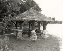 Vue générale du belvédère, qui montre le toit octogonal à couverture de bardeaux, les piliers en moellons bruts, et les poteaux et consoles en rondins écorcés, 1992.; Parks Canada Agency / Agence Parcs Canada / Historica Resources Ltd., 1992.