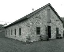 Corner view of the Foundry, showing the exterior walls of rubblework, the placement of the simply detailed door and windows, with voussoirs and dressed stone sills, 1989.; Public Works and Government Services Canada / Travaux publics et Services gouvernementaux Canada, 1989.