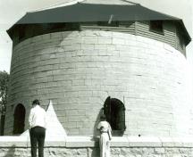 Vue de la façade ouest de la tour Martello Murney, qui montre les murs en calcaire et les portes de caronade à voûte ronde garnies de volets de fer, 1991.; Parks Canada Agency / Agence Parcs Canada, 1991.