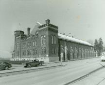 Corner view of the Armoury, showing the masonry work with medieval military detailing, including buttresses, dentilated stringcourses, corbelling and crenellations, 1989.; Department of National Defence / Ministère de la Défense nationale, 1989.