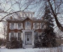 Vue de la façade principale de la maison Bentley, qui montre la porte centrale mise en évidence par un porche délicat soutenu par des colonnettes délicates à l’italienne, 1992.; Public Works and Government Services Canada / Travaux publics et Services gouvernementaux Canada, 1992.