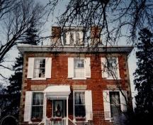 Vue arrière de la maison Bentley, qui montre les murs extérieurs de brique rouge qui contraste avec la brique pâle utilisée pour l’encadrement des fenêtres et pour les pierres d’angle, 1992.; Public Works and Government Services Canada / Travaux publics et Services gouvernementaux Canada, 1992.