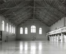 View of the Armoury, showing the large, interior drill hall space with its Fink trusses and full-length viewing gallery, 1992.; Ministère de la Défense nationale / Department of National Defence, 1992