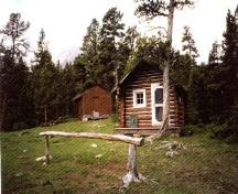 Vue de la façade du chalet de gardes de parc de Fourpoint, où l'on peut apercevoir le prolongement du haut, qui forme une légère saillie au-dessus du porche et la peinture rouge brunâtre de l’extérieur, avec les détails de couleur pâle, 1996.; Parks Canada Agency / Agence Parcs Canada, 1996.