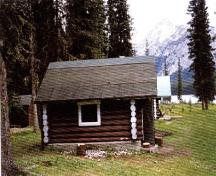 Façade latérale de la sellerie du chalet des gardes du parc du lac Jacques, qui montre la teinture brune qui couvre les rondins avec leurs extrémités blanchies à la chaux.; Parks Canada Agency/ Agence Parcs Canada, 1996.