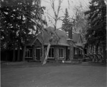 Vue générale du pavillon de golf, qui montre les murs en rondins écorcés et les nombreux détails en pierre, 1986.; Parks Canada Agency / Agence Parcs Canada, Mills, 1986.