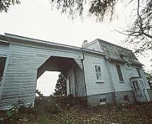 General view of Building 43, showing a covered passageway that connects a mansard roofed one-storey residence to a gable roofed shed, circa 2004.; Parks Canada Agency / Agence Parcs Canada, circa / vers 2004.