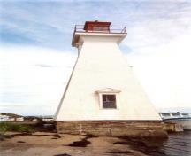 Vue générale du phare Mabou démontrant l'élévation ouest et sa construction robuste et massive ainsi que ses matériaux durables, comme l’ossature en bois, la fondation en béton armé et le parement de blanches embouvetées, 2002.; Public Works Canada / Ministère des Travaux publics, 2002.