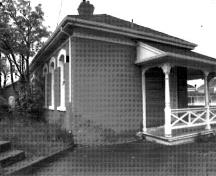 Corner view of the northeast elevation of Building 29, showing the the verandah with decorative woodwork and railing on the main elevation, 1989.; Parks Canada Agency/Agence Parcs Canada, I. Doull, 1989.