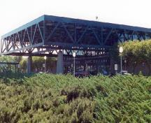 Vue général de la gare de VIA Rail démontrant la structure massive de béton à piliers et à poutres qui soutient son toit à ossature spatiale, et qui s'étend pour former des auvents devant et derrière l'édifice.; Parks Canada Agency / Agence Parcs Canada, n.d.