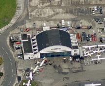 Vue aérienne du Hangar d'Harbour Air, bâtiment T-018, montrant la simplicité et l’asymétrie de la façade principale, et de la tour de deux étages, à l’angle sud-ouest, qui comporte un toit plat et une composition bien équilibrée d’étroites fenêtres vertic; Microsoft Bing Maps, 2011.