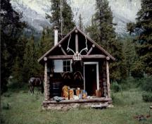 Vue de la façade du chalet de patrouille des gardes du parc de Topaz, où l'on peut apercevoir le toit à deux versants et le porche ouvert en rondins munis de supports pour les pannes de la ferme et les poteaux à l’extrémité du pignon, 1997.; Parks Canada Agency / Agence Parcs Canada, 1997.