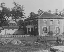 Vue générale de la Résidence de l'amiral et Ancienne maison du magasinier naval, montrant la forme rectangulaire de l’édifice à deux étages qui est réalisé en brique et en pierre.; British Columbia Archives and Records Service, / Archives et Service des documents de la Colombie-Britannique, HP 7856.