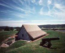 Vue de coin de la Poudrière sud démontrant son volume rectangulaire bas avec un toit à pignon et avant-toit avec évasement prononcé, 1977.; Parks Canada Agency / Agence Parcs Canada, T. Grant, 1977